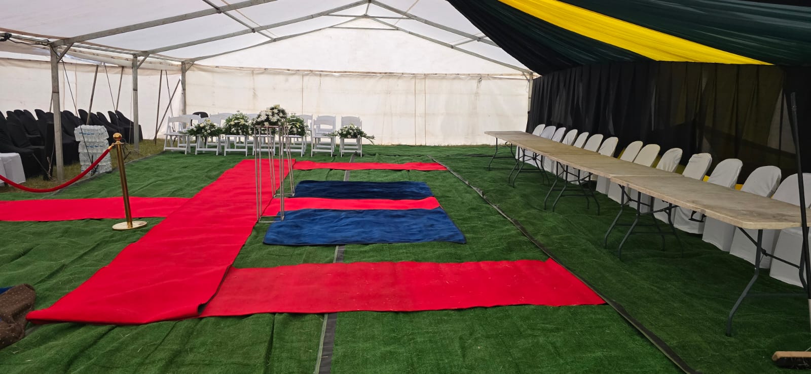 Funeral tent setup with green carpet and red walkways