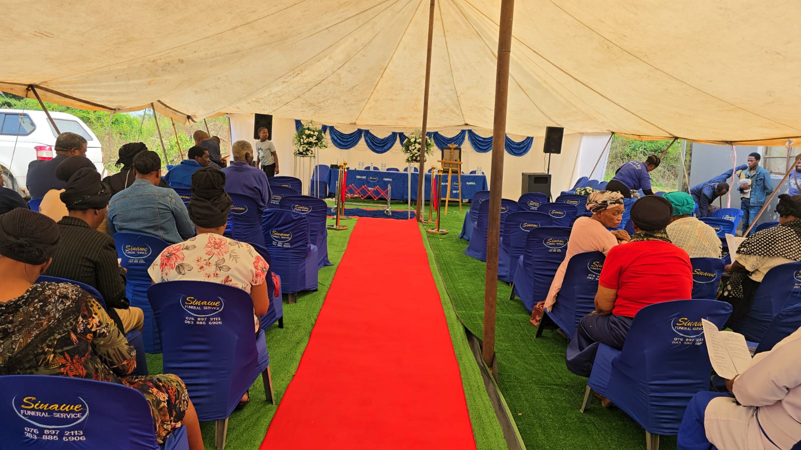 Guests seated under a Sinawee funeral tent with blue chairs